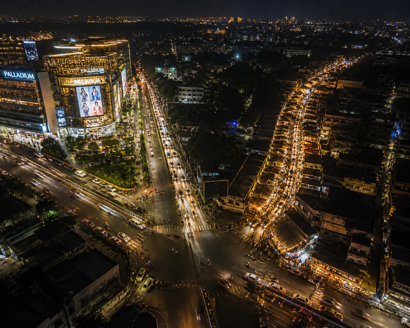 Aerial night view of a modern shopping mall and busy traffic intersection contrasted with a dense older city street